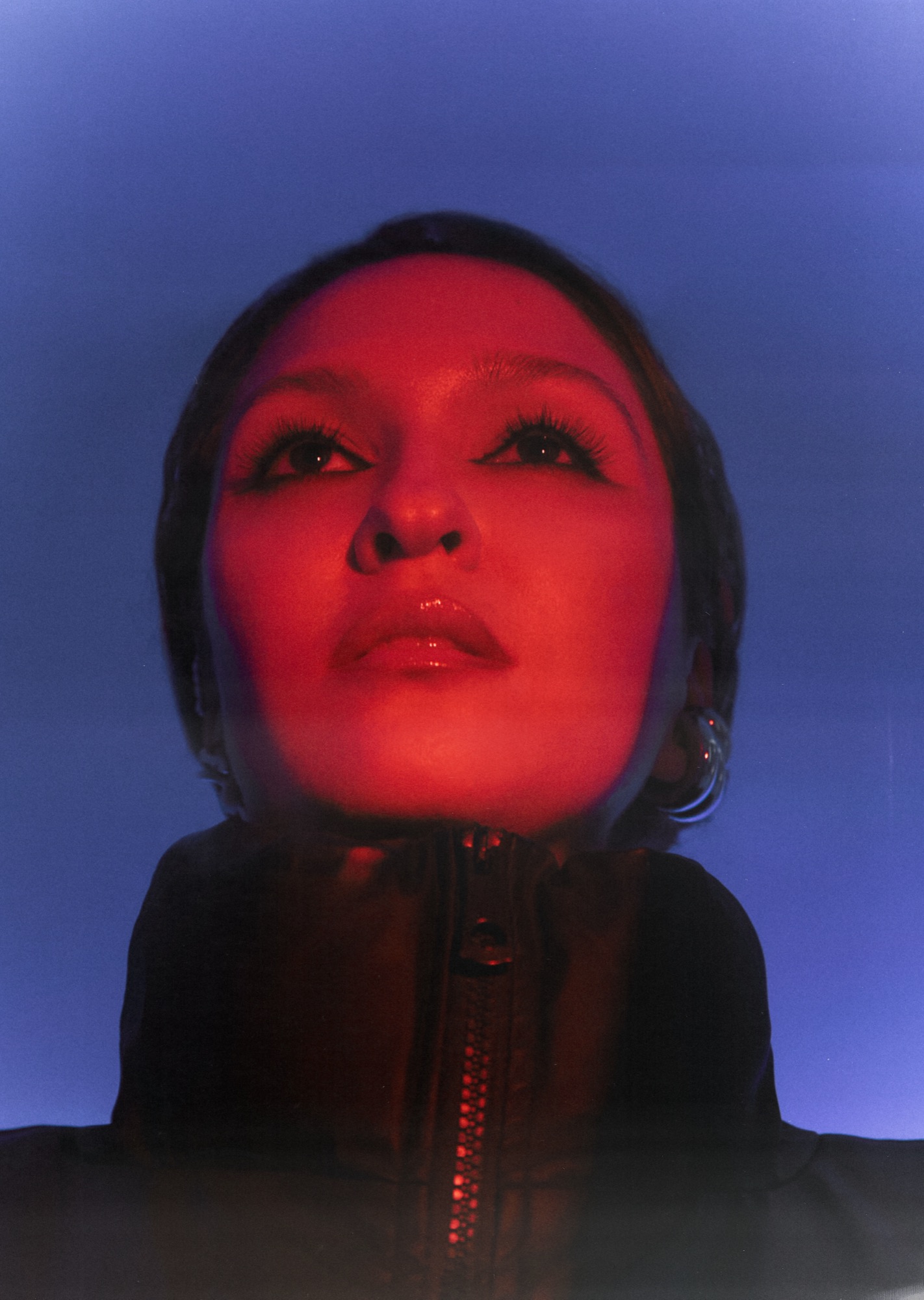 AYGYUL in an oversized black jacket against a blue backdrop